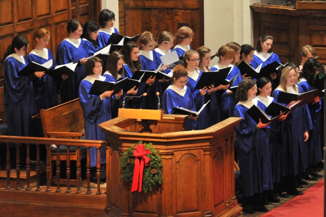 A group of choir singers in blue robes, in Mead Chapel, with a holiday wreath