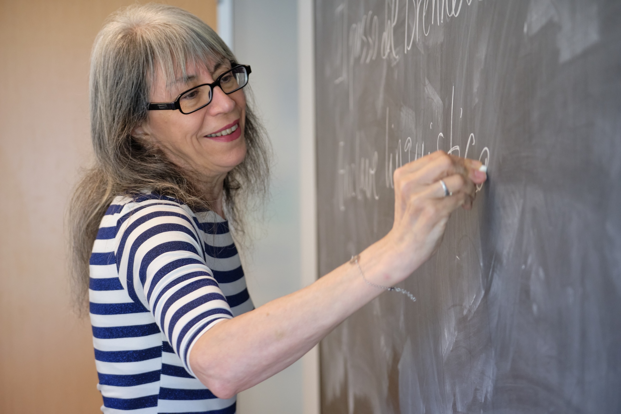 A teacher smiles as she writes in Italian on the blackboard.