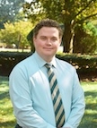 A man in a shirt and tie smiles at the camera.