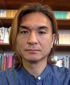 Nobuaki is wearing a blue shirt and is pictured in front of books.