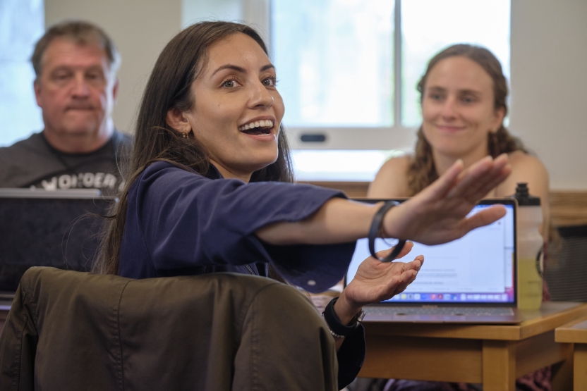 A woman shares something in class- she gestures toward the board. 