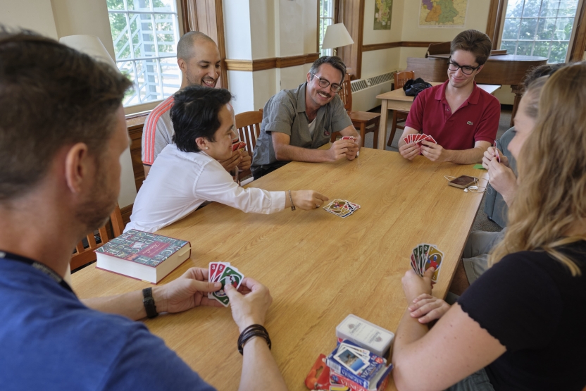 A group of friends plays uno at a wooden table, smiling. 