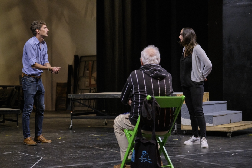 Two students rehearse a play as their director watches from a chair. 