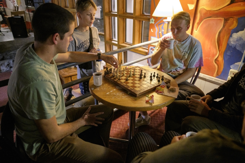Students drink tea and play chess in a lamplit recreation room. 