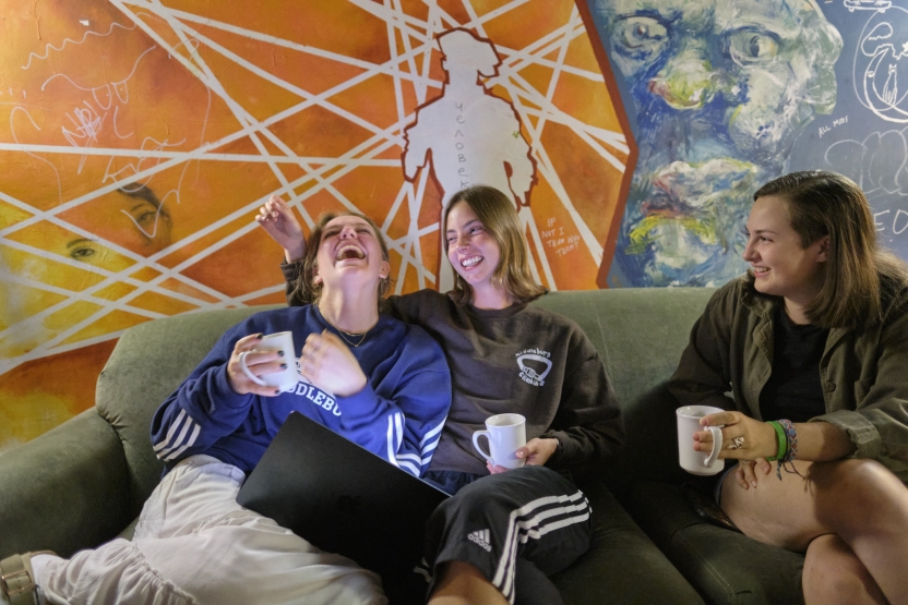 Students sit on a couch drinking tea, smiling and laughing.