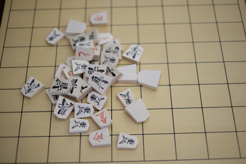 Tiles with black and red lettering in Japanese are in a pile on top of a grid on a table.