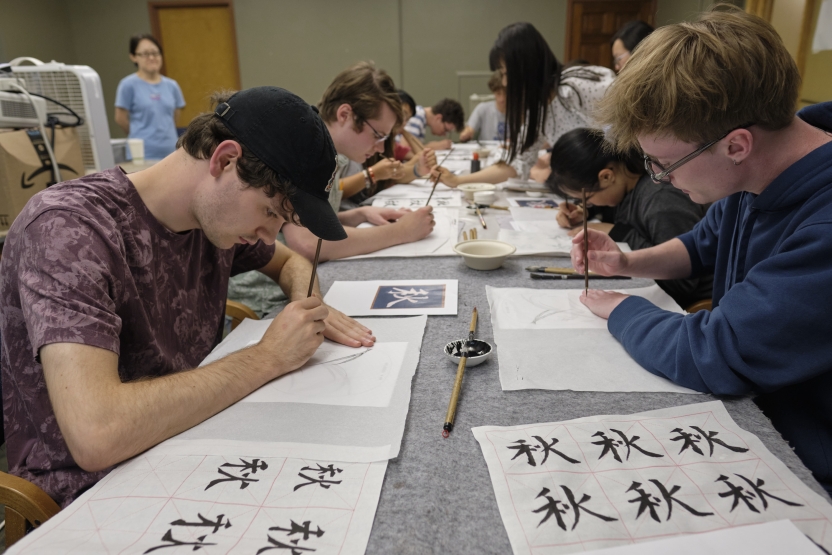 Students sit at a table practicing their calligraphy skills