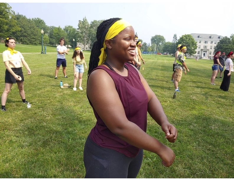 A student smiles as she participates in a group activity outside, flexing her arms.