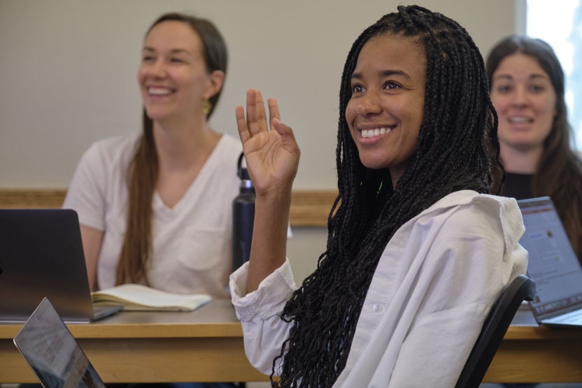 A student smiles as she raises her hands in class. 