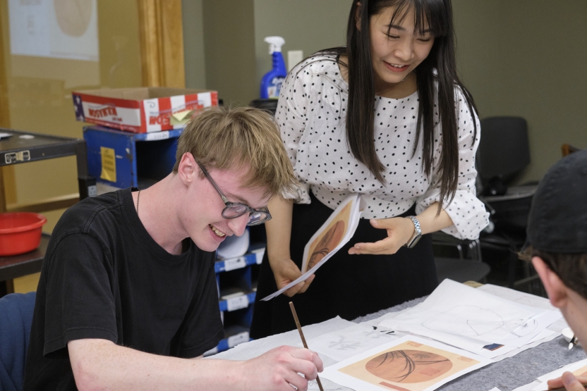 A teacher helps her student with his Chinese art. 
