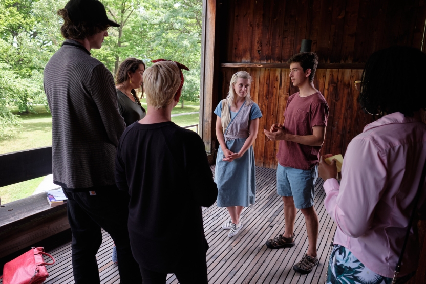 Students stand in an indoor outdoor space, speaking to each other in a group activity.