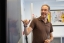 A teacher smiles as he gestures at a blackboard.