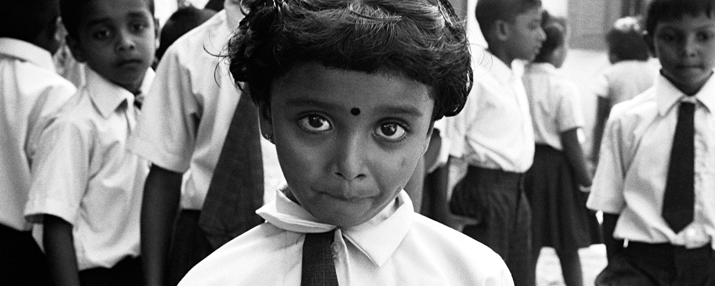 a close up of a Sri Lankan school girl with her hair pinned in barrettes; several other school children stand behind her