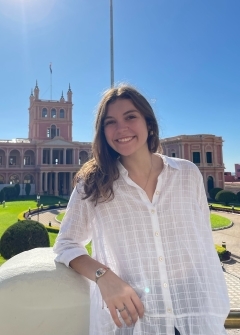 Student smiling in front of a building in the sunshine