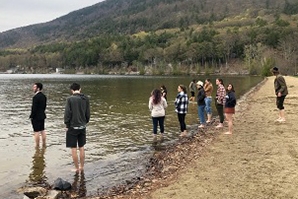 Several students stand on a lake beach.