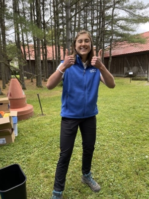 Emma Henry stands outside, smiling with two thumbs up, wearing a blue vest.