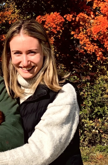 A person with blond hair, smiling against Fall Foliage