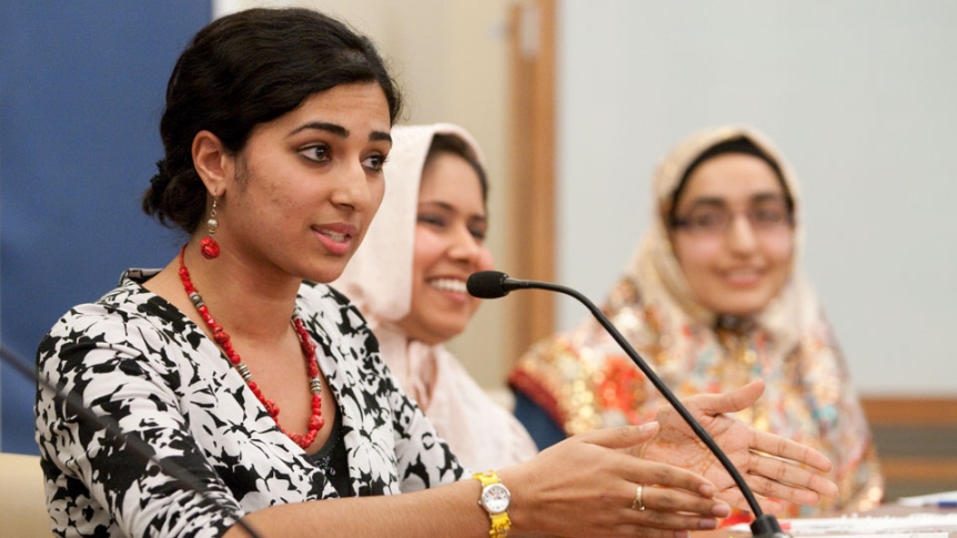 A woman speaks into a microphone as part of an international meeting.