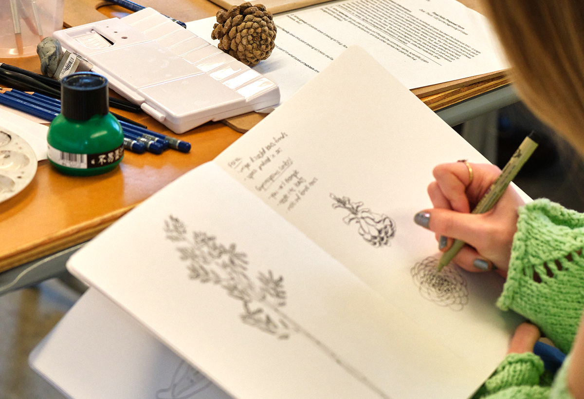 Over the shoulder photo of a student sketching in a book.