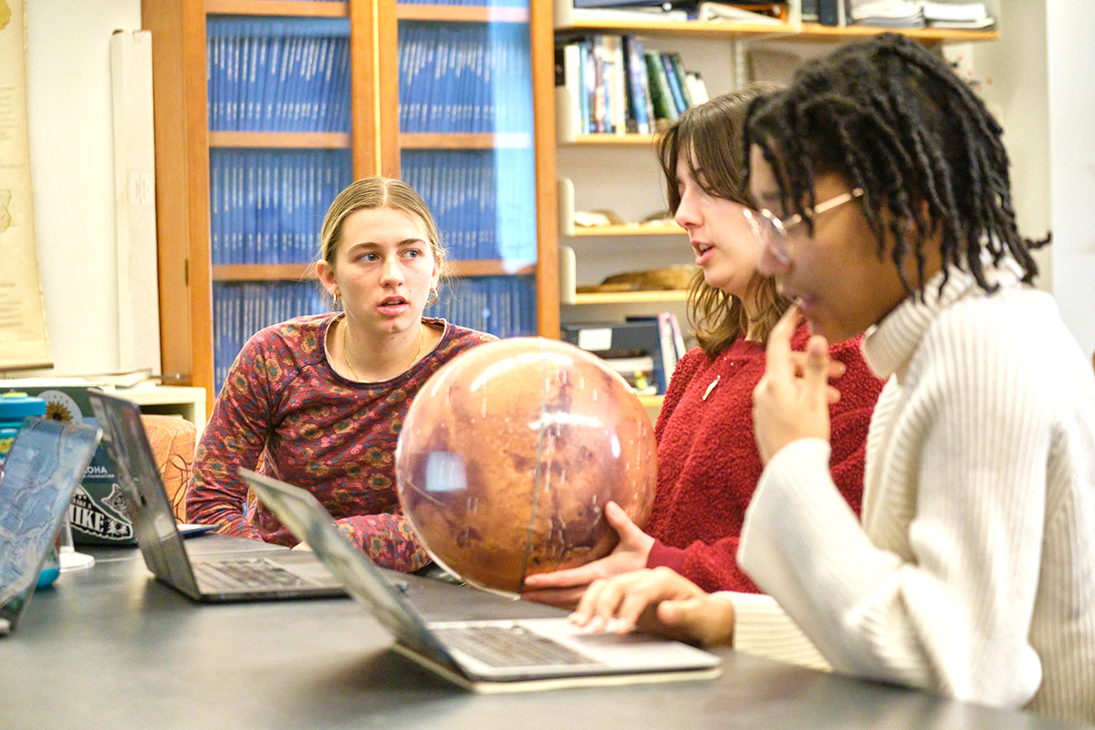 Students in a classroom discuss a model of a planet.