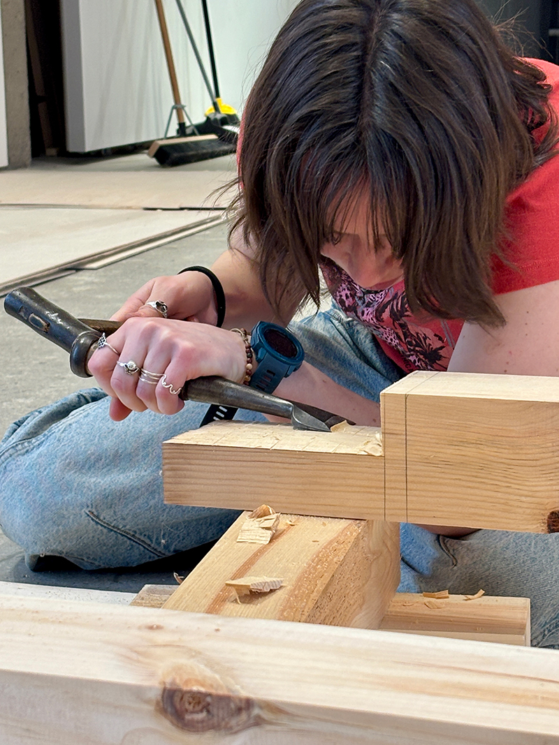 A student works on a timber with chisel and hammer