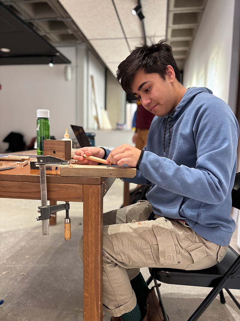A student hand mills a wooden pin for a timber structure.