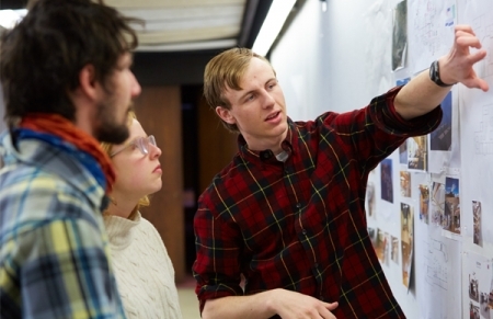 A man points to a whiteboard covered in photos while another man and woman watch.