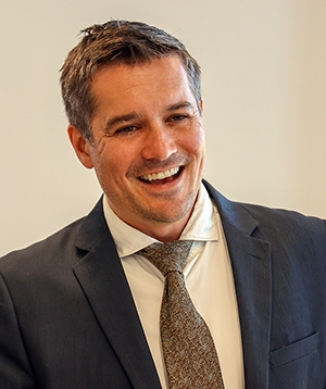 Photo of Middlebury Associate Professor Thor Sawin smiling at lectern, wearing coat and tie.