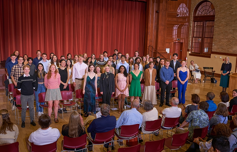 A group of students in a large room standing and smiling at the audience.