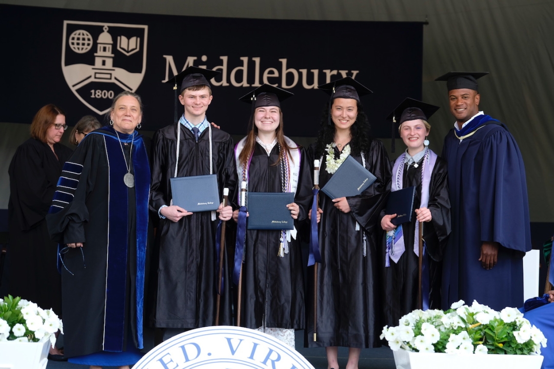 Students and administrators stand at the front of the stage during commencement