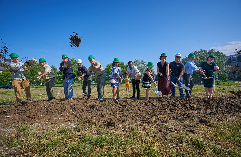 A group of people in hardhats throw soil at a groundbreaking.