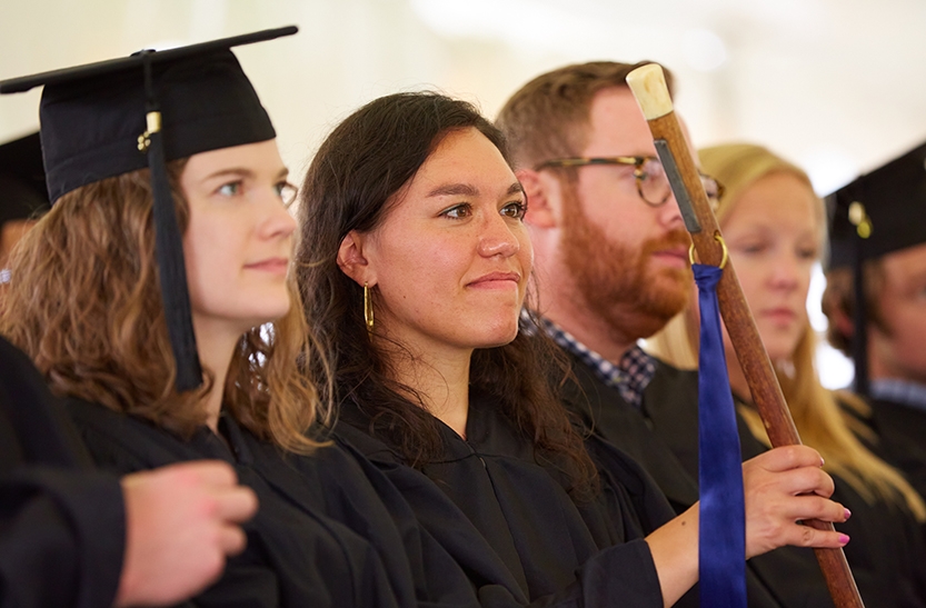 Graduates in academic regalia sit in a row during a commencement ceremony.