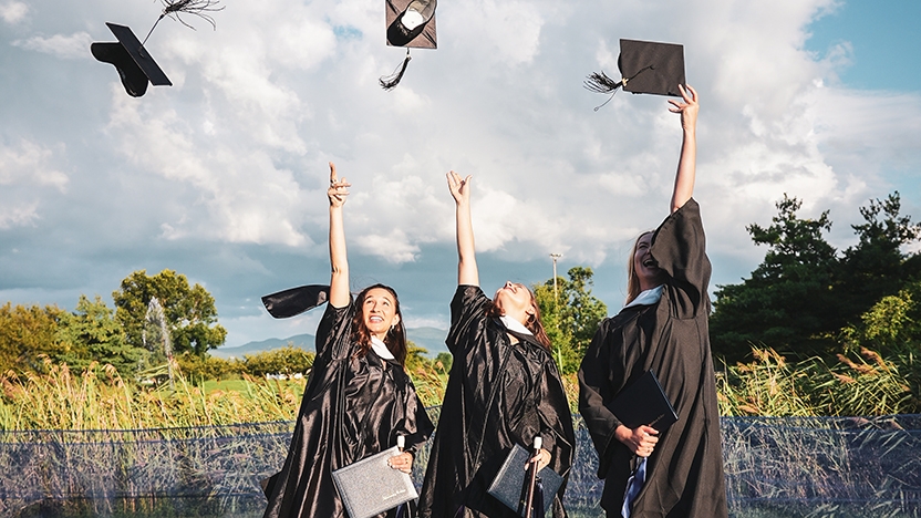 Three LS students throwing their caps in the air.