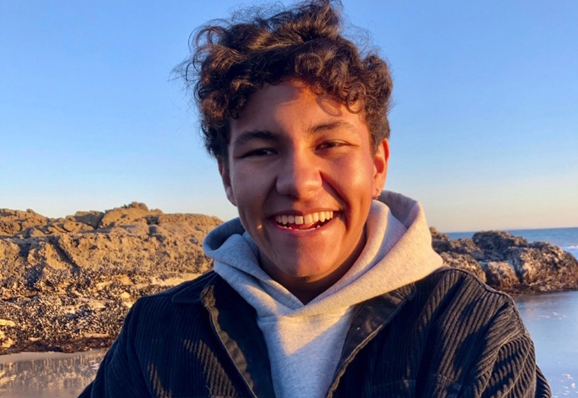 A student smiles at the camera outside with blue sky behind.