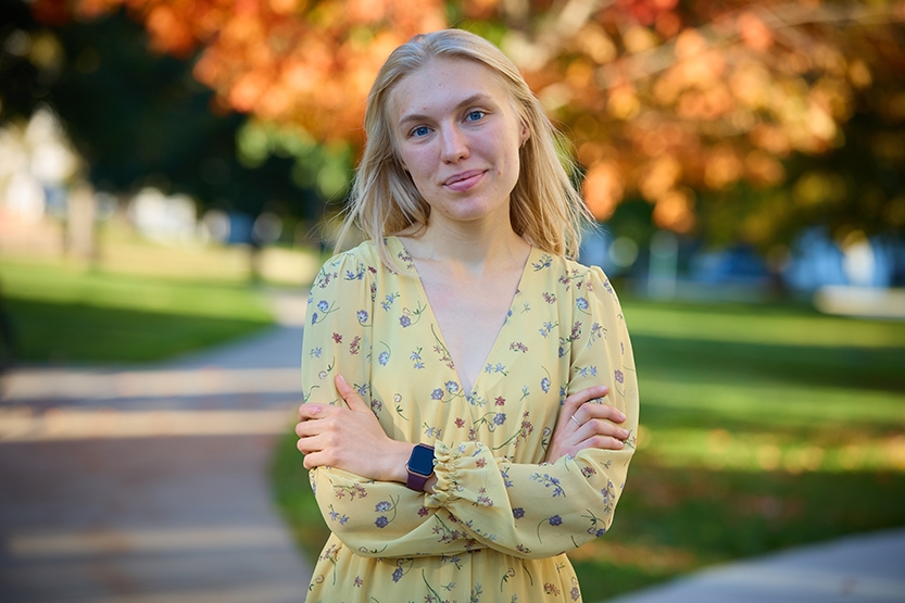 Student stands on campus with arms folded