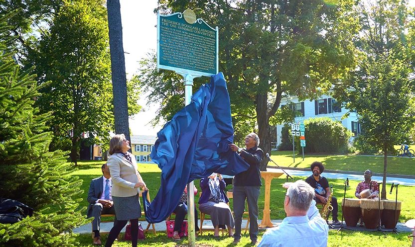 Two people unveil a historic plaque marker outside.