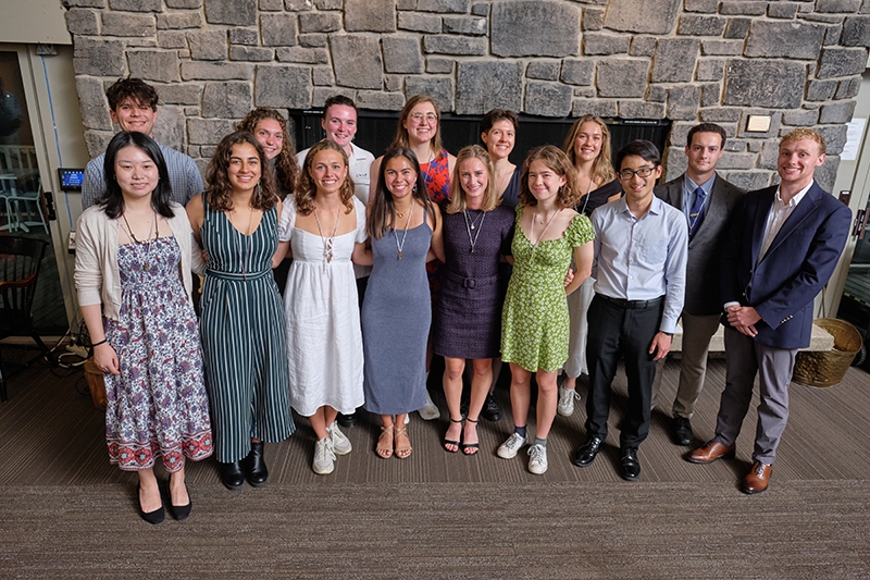 A small group of students poses for a photo in front of a fireplace.