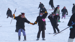 Two students in caps and gowns ski down a snowy slope.