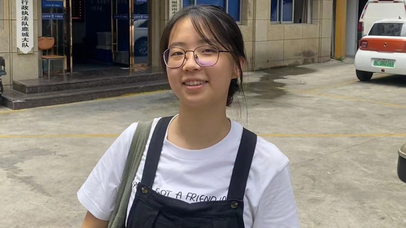 Student intern stands on a street with cars in the background.