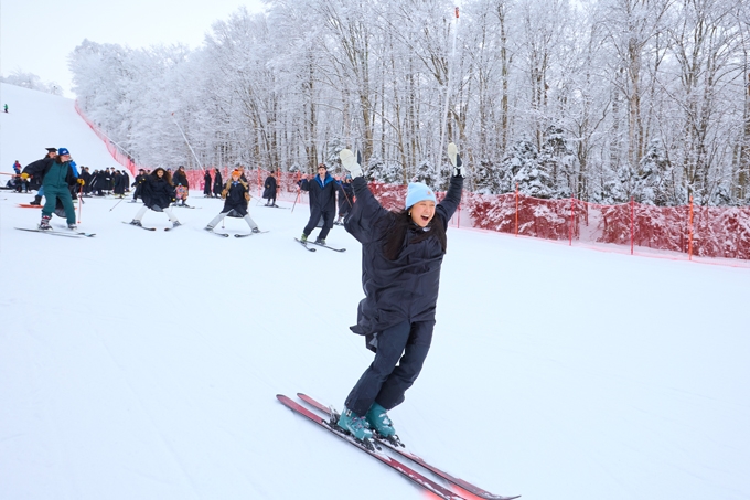 A midyear graduate skis down the Snowbowl with arms up in celebration.