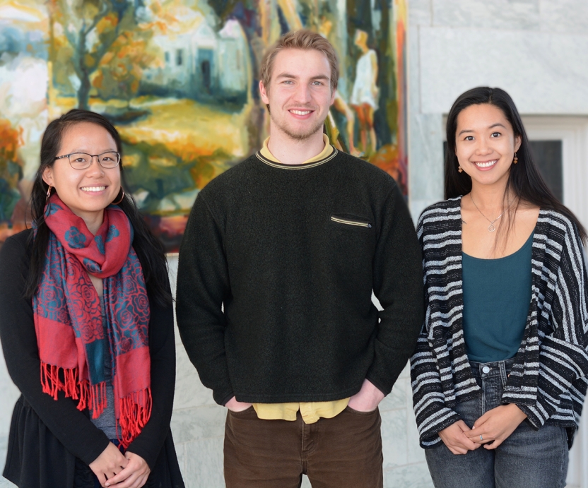 Three students pose in front of a painting.