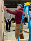 Man in red sweatshirt measures a wall of a timber structure.