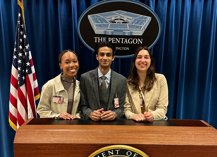 Three students stand and smile at a lectern at the Pentagon.