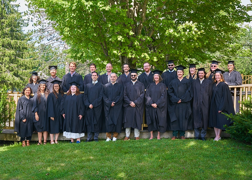 Students in academic regalia pose for a group photo outside.