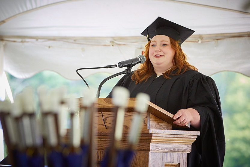 A student in academic regalia speaks at a lectern during commencement.