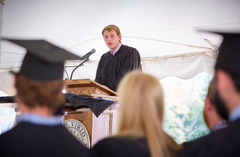 A student in academic regalia speaks at a lectern during commencement.