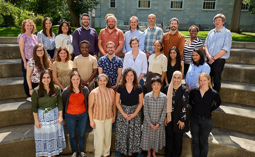 A large group of faculty members poses for a group photo outdoors.