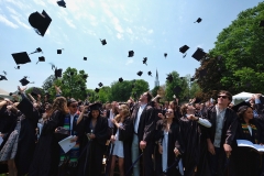 A crowd of students in graduation caps and gowns throws their caps in the air.