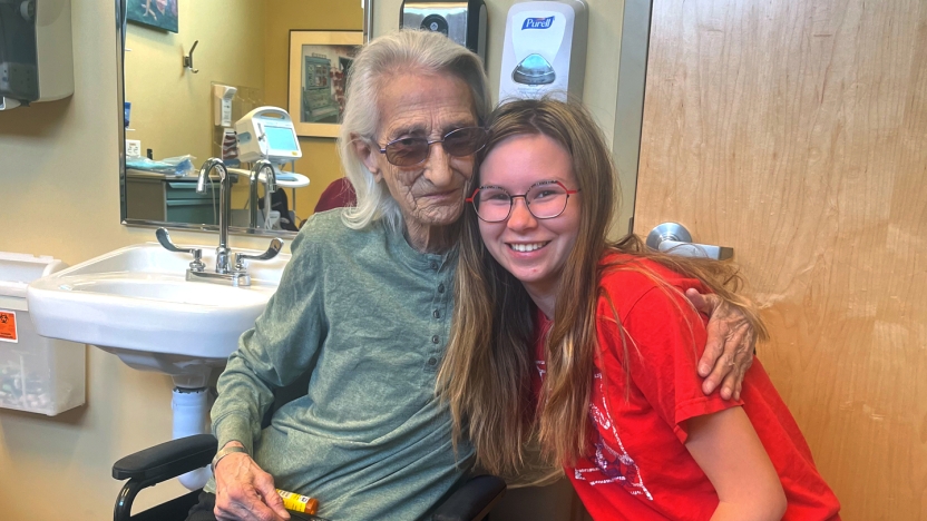 A student intern poses for a photo with a patient in a wheelchair.