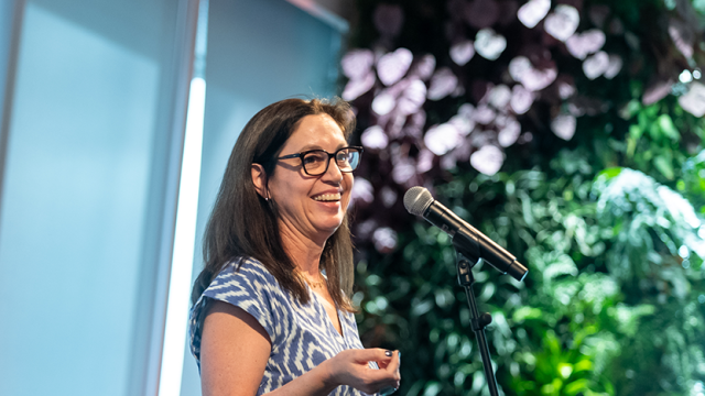 Ninive Calegari at the mic in a well-lit room with green plants